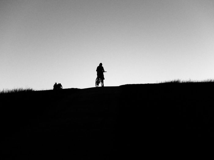 Silhouette man bicycling on field against clear sky