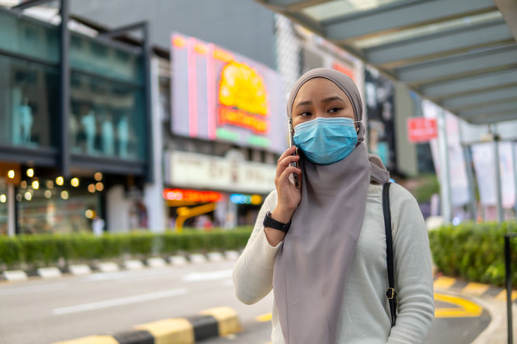 Young woman wearing mask talking on phone while standing outdoors