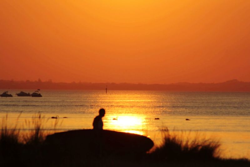 Silhouette man looking at sea against orange sky
