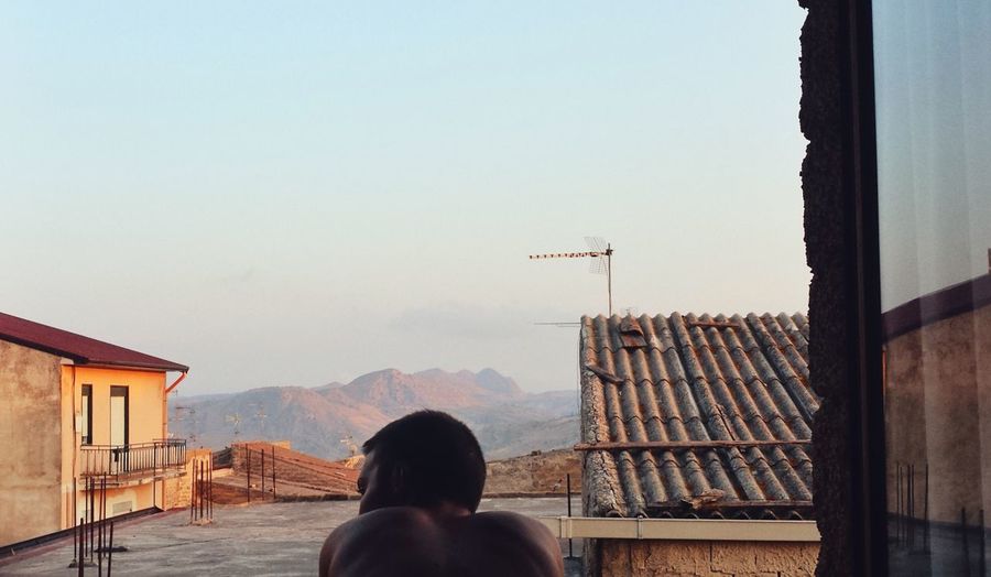 Rear view of shirtless man at window against sky