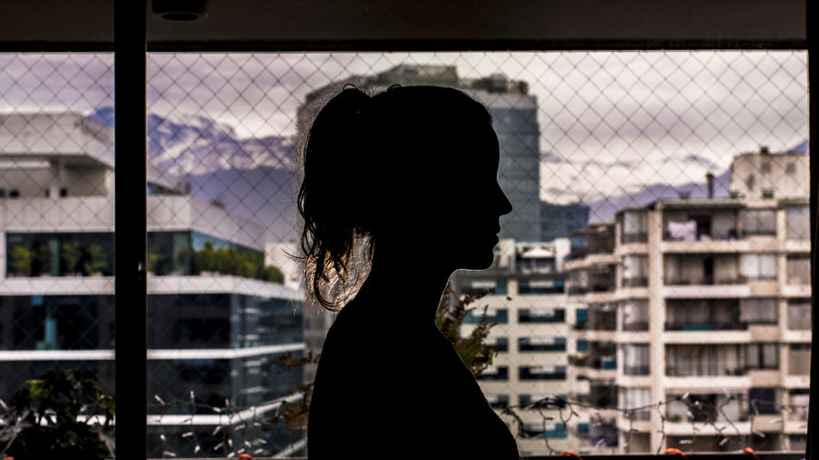 Side view of silhouette woman standing by chainlink fence