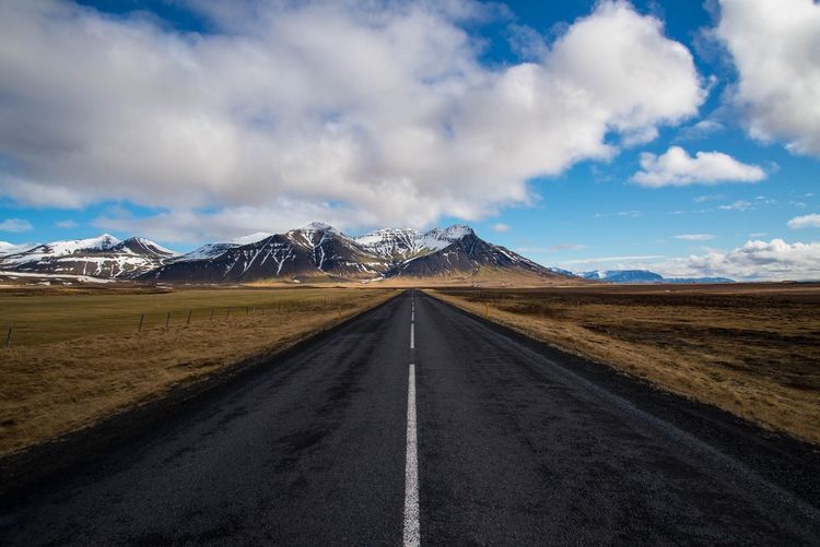 Empty road amidst landscape against sky leading towards mountain