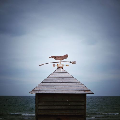 Weather vane on roof by sea against sky