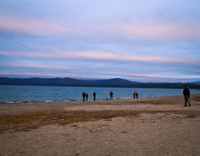 People at beach against cloudy sky during sunset