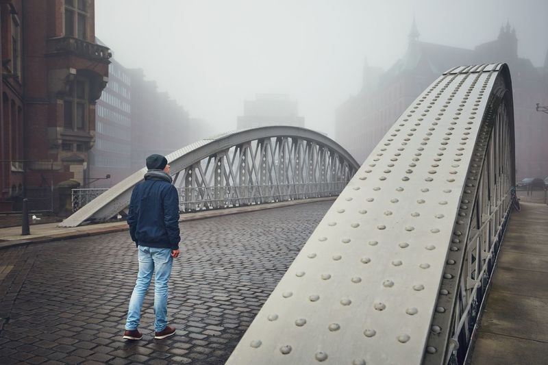 Rear view of man walking on bridge in city