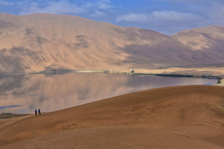 1153 sumu barun jaran lake in badain jaran desert-dark water reflecting cloudy sky and dunes. china.