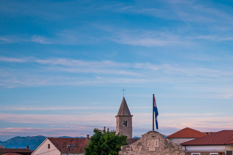 Skyline of town nin in croatia with church tower, red roofs and croatian flag on a blue sky.