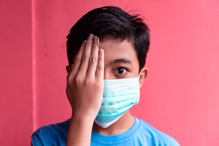 Portrait of boy covering face against red background
