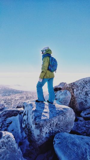 Woman standing on rock against blue sky during winter