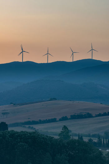 Wind turbines on land against sky during sunrise