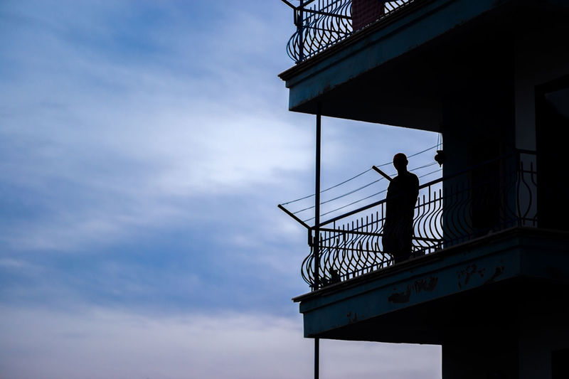 Low angle view of silhouette man standing on balcony against sky at dusk
