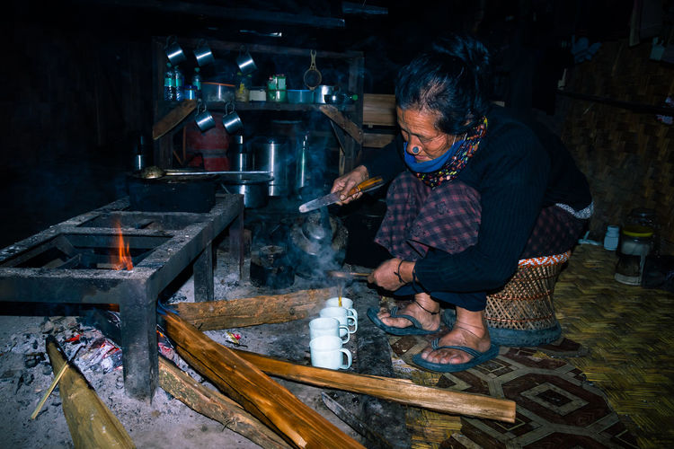 Apatani tribal lady making tea at her home near fire place at evening
