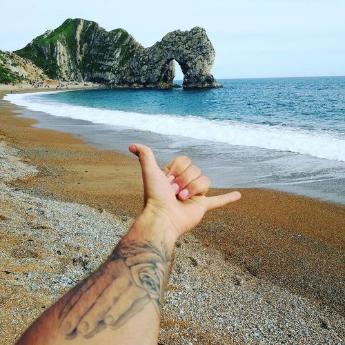 Cropped hand of man gesturing shaka sign on shore at beach
