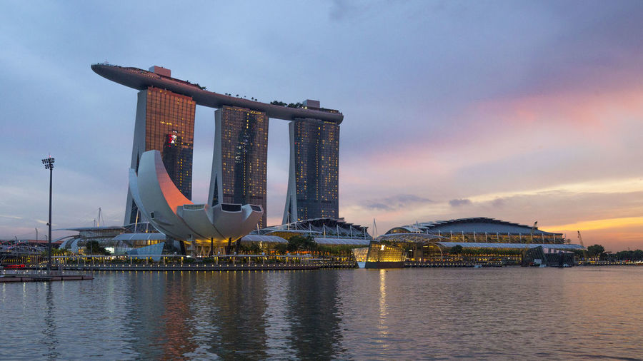 Marina bay sands by bay of water in city during sunset
