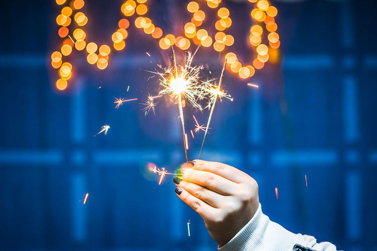 Cropped hand of woman holding illuminated sparklers at night