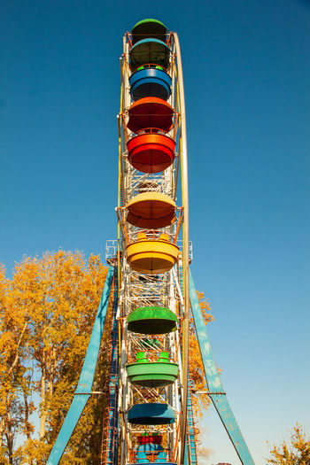 An old ferris wheel with bright booths against a blue sky
