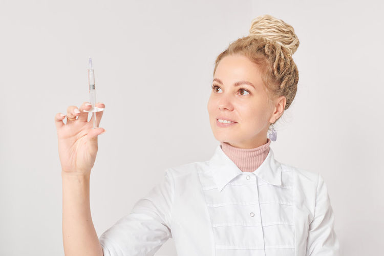 Portrait of young woman holding syringe against white background