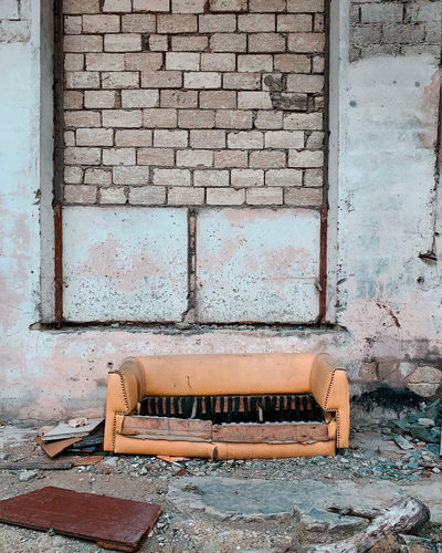 Abandoned sofa against brick wall of old building