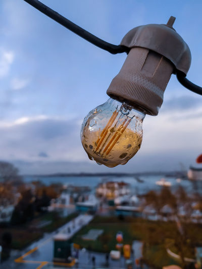 Close-up of light bulb hanging against buildings