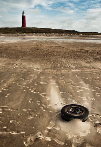 Abandoned wheel at beach by lighthouse against sky
