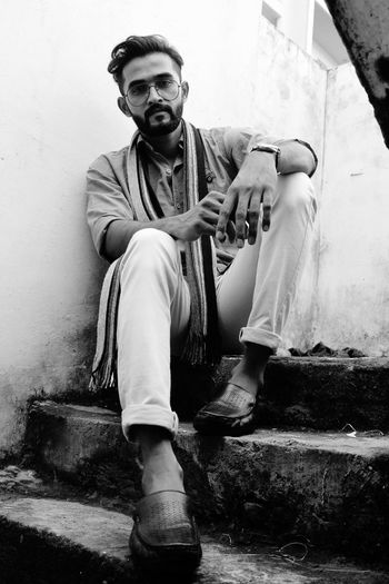 Low angle portrait of young man sitting on steps against wall