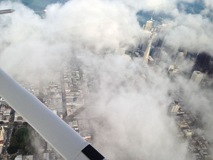 Cropped image of airplane over clouds covering cityscape