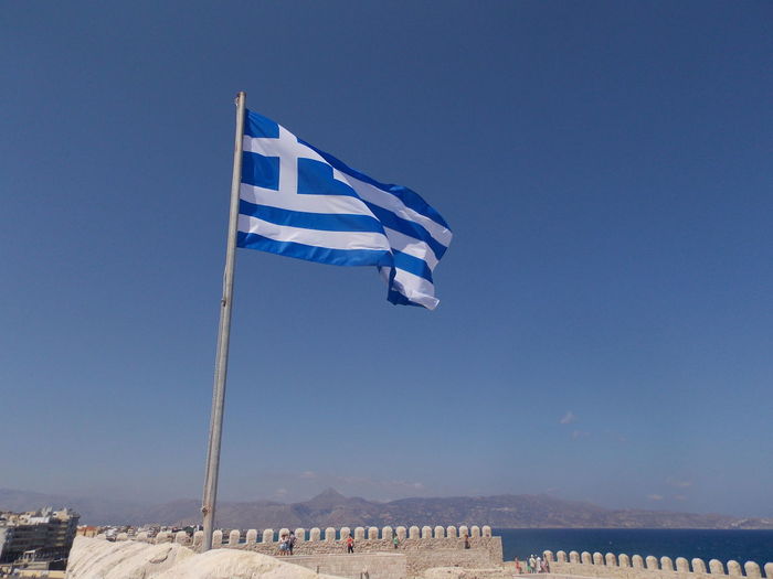 Low angle view of greek flag against clear blue sky