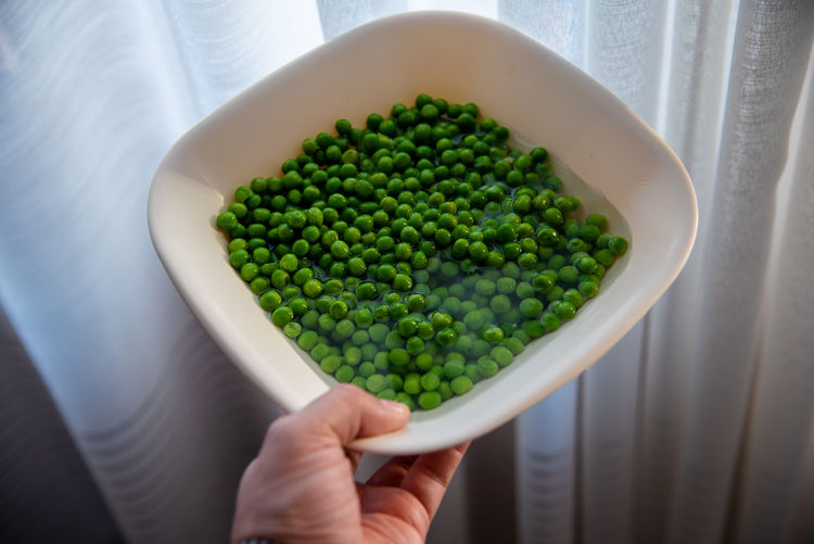 Cropped hand of person holding green peas in bowl