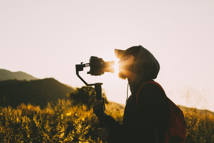 Man photographing camera on field against sky during sunset