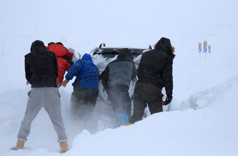 Rear view of people pushing car stuck in snowdrift