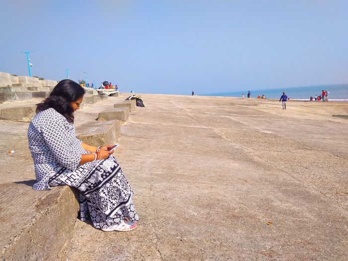 Side view of woman sitting at beach against clear sky