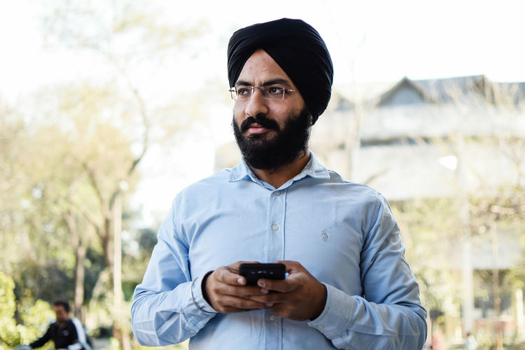 Low angle view of mid adult man wearing turban while holding mobile