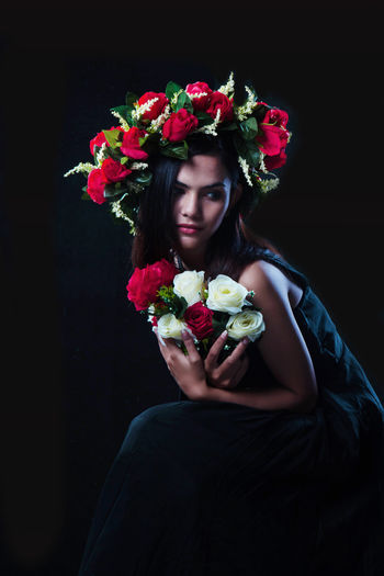 Thoughtful female model wearing flowers while sitting against black background