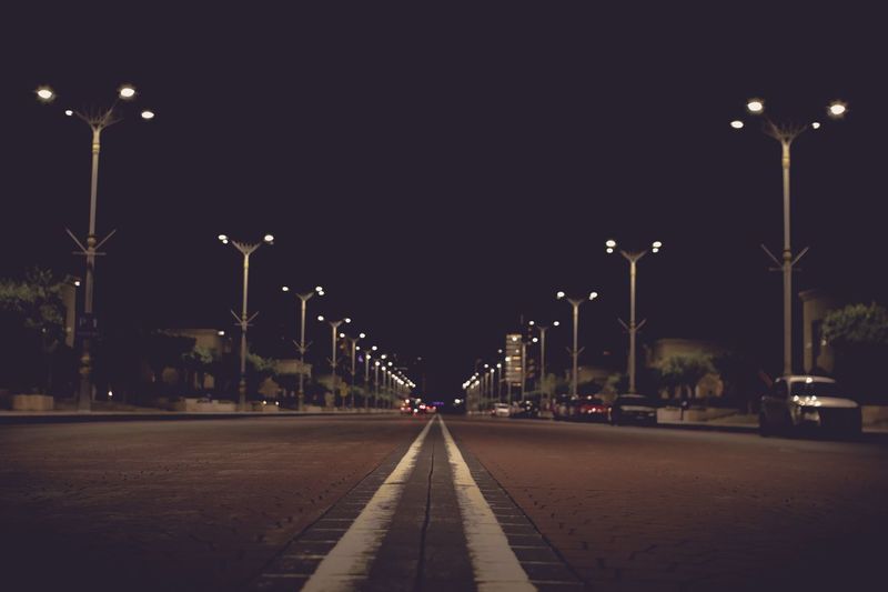 Empty road against illuminated street lights in city at night