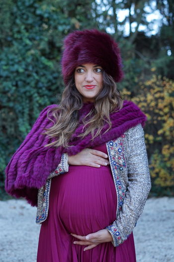 Smiling pregnant woman in warm clothing standing outdoors