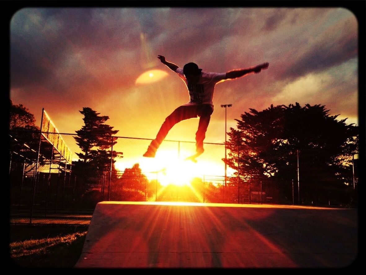 transfer print, auto post production filter, sunset, sky, sun, mid-air, full length, jumping, sunbeam, tree, sunlight, lens flare, silhouette, arms raised, arms outstretched, leisure activity, cloud - sky, lifestyles