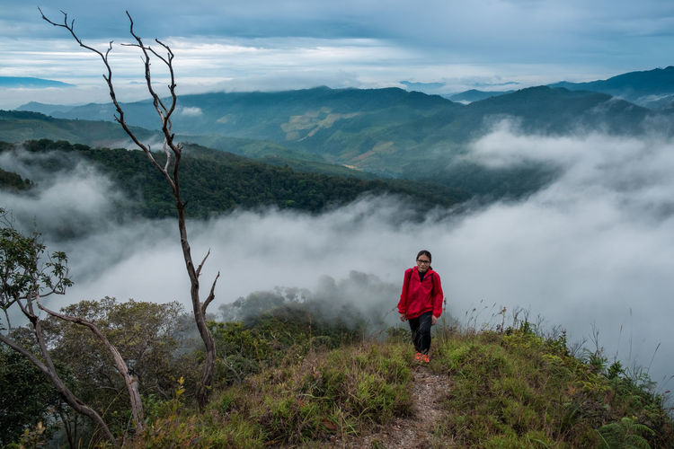 Woman walking on mountain against cloudy sky
