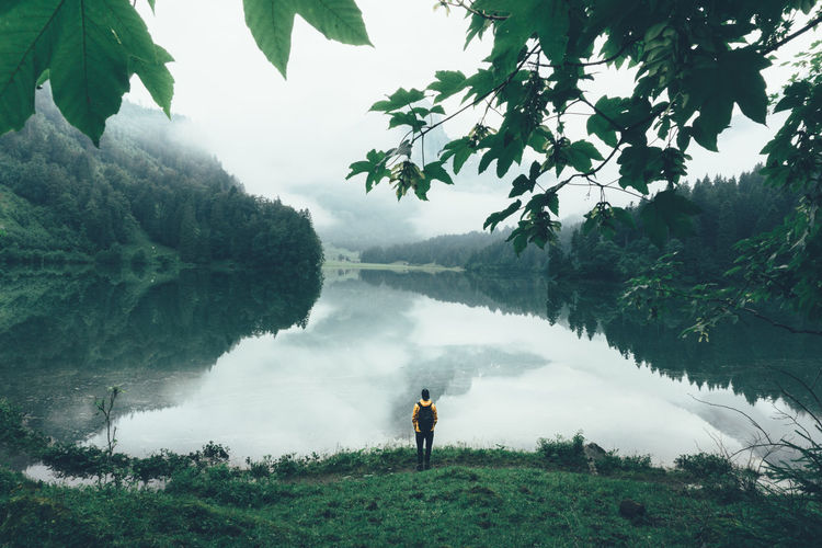 High angle view of man with backpack standing by lake during foggy weather