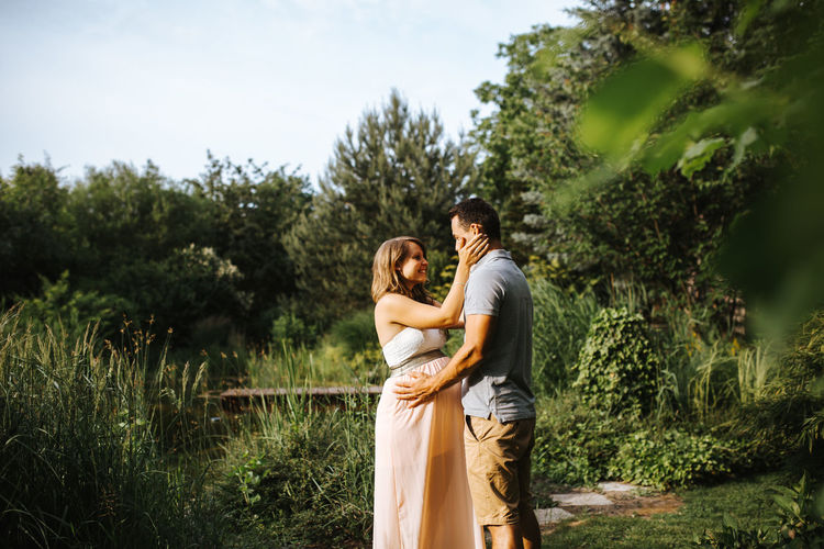 Side view of man kissing pregnant wife while standing amidst plants
