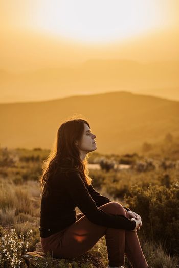 Side view of young woman looking away at sunset