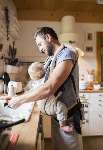 Happy father with baby in baby carrier doing the dishes