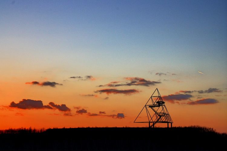 Silhouette of electricity pylon on field against sky during sunset