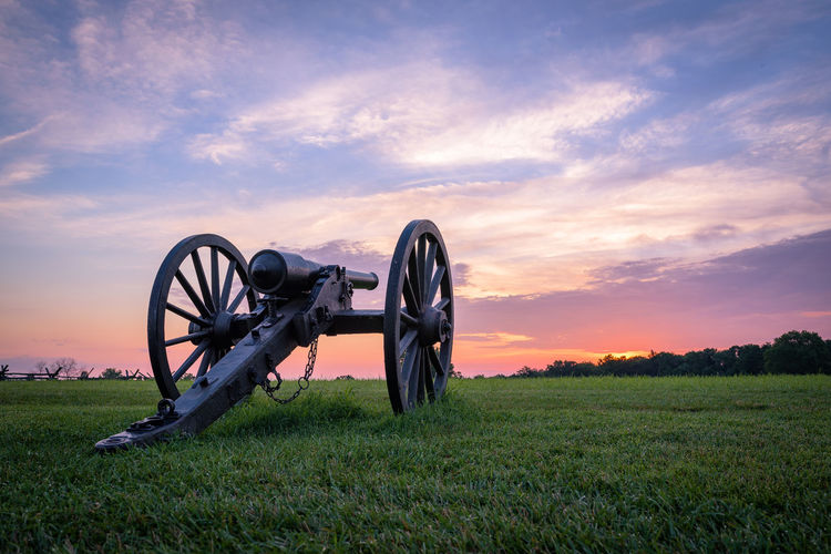 Cannon on field against sky during sunset