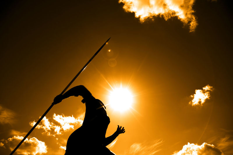 Low angle view of silhouette man with javelin against sky during sunset