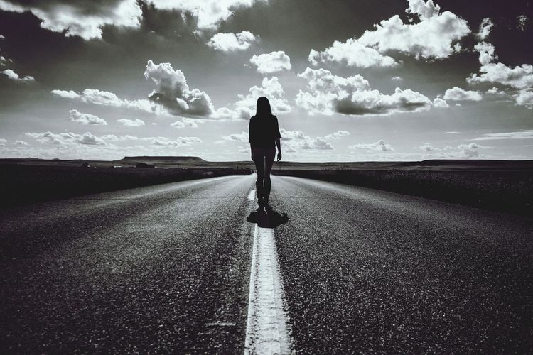 Silhouette woman walking on road against sky