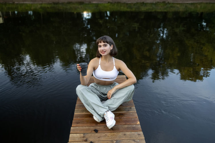 Portrait of young woman sitting on lake