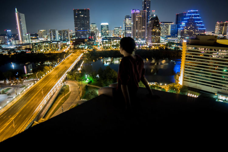 Girl on terrace looking at illuminated cityscape
