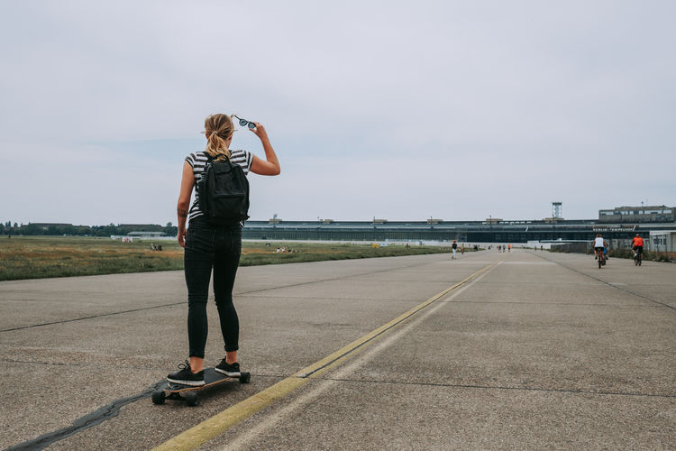 Rear view of woman standing on skateboard against sky