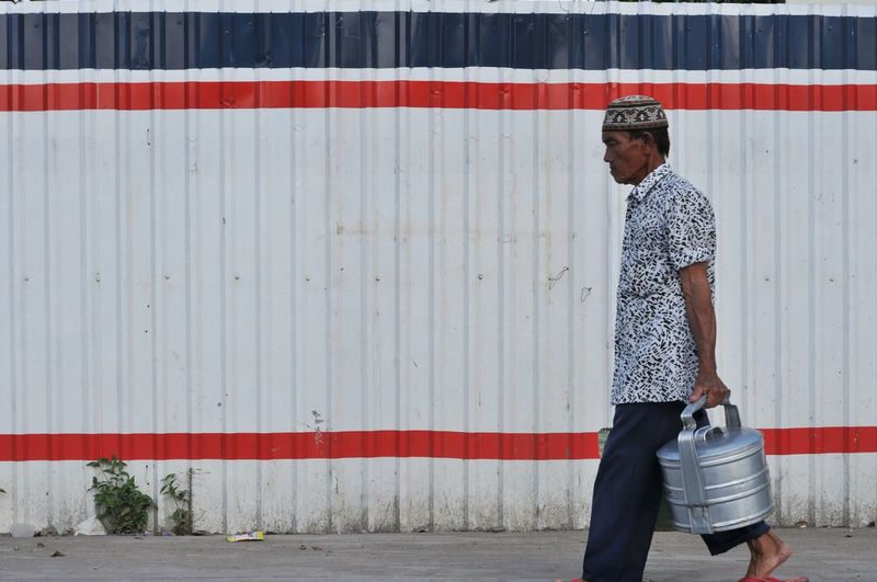 Side view of man with containers walking on footpath