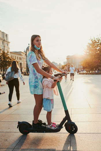 Teenager girl and her sister preschooler riding an electric scooter in the city center